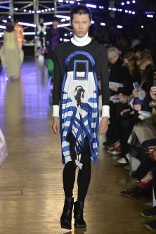 Model walking down catwalk wearing blue and black outfit