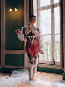 Female model with cropped hair and tattoos wearing a white mesh dress covered in blood