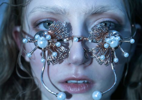 Female model closeup wearing gold flower shaped glasses with pearls