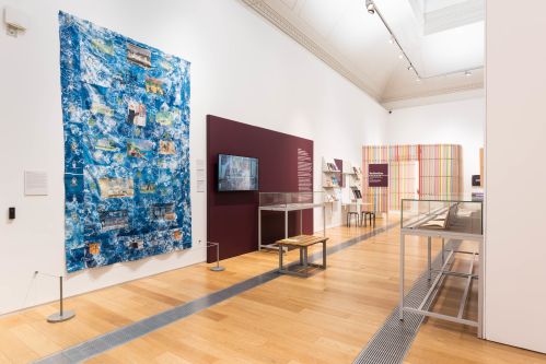 A wide shot of an exhibition space with a large blue hanging textile and other artworks