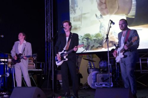 Photograph of three men on stage in suits, performing with guitars