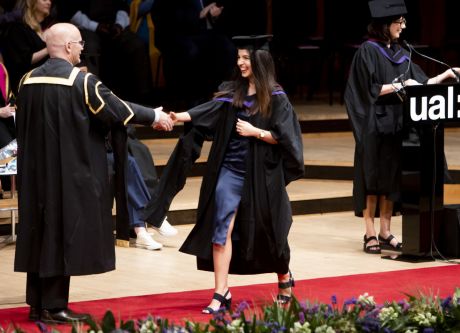 Graduate receiving her award on stage and shaking hands.