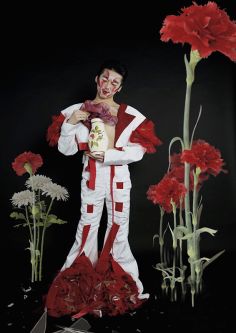 Male model in a white suit with red inserts with large poppies in the background