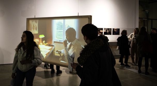 figures in a gallery looking at a film projection of a woman