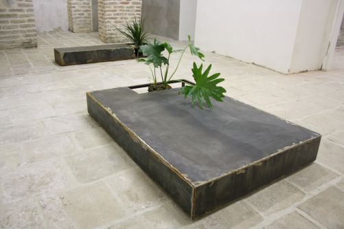 A compartmentalized metal box with two plants in, in a tiled courtyard