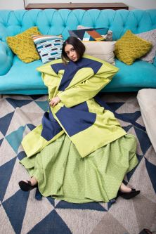 Model wearing Baga Dress and Lori Trench Coat lying next to sofa