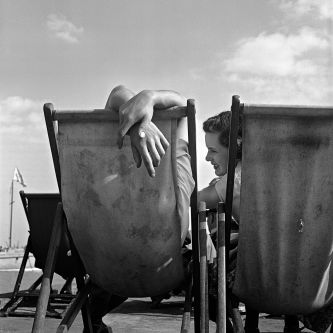 Black and white photo of two people sitting on a deck chair, taken from behind.
