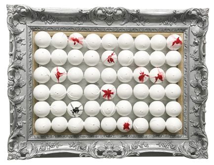 Daniela's artwork called Mirror Mirror. A silver carved frame with rows of white ping pong balls, some with red paint, and one with black paint marked on. 