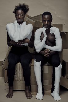 two models sitting on cardboard boxes, wearing artefact limbs in contradicting poses