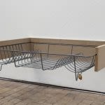 Photograph of an art installation detail. a wooden shelf consisting only of two wooden sides and a metal dish draining holder slotted into it