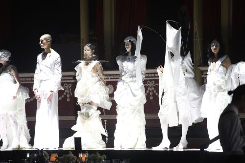 Models wearing white garments standing along catwalk