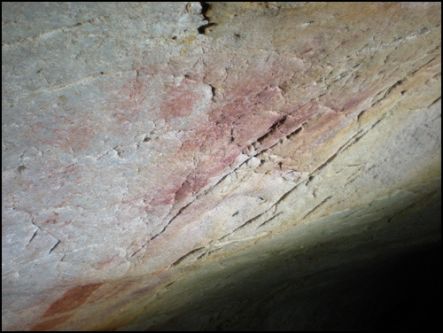 A close up of a paleolithic hand stencil on a cave wall in red pigment