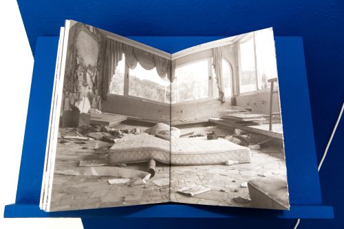 A black and white photograph showing a destroyed room and a bed.