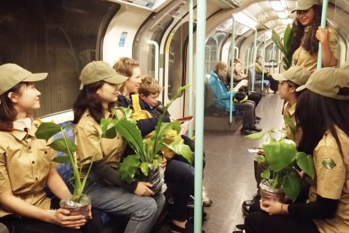 Students dressed as park rangers on a tube train carrying plants and talking to passengers