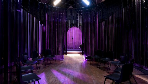 An dark interior installation lit up in purple with lights, chairs and an archway visible