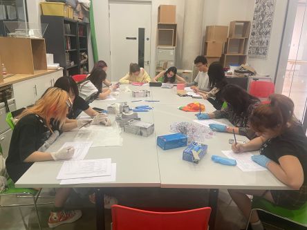 A group of students seated around a table wearing archival gloves and working on a project
