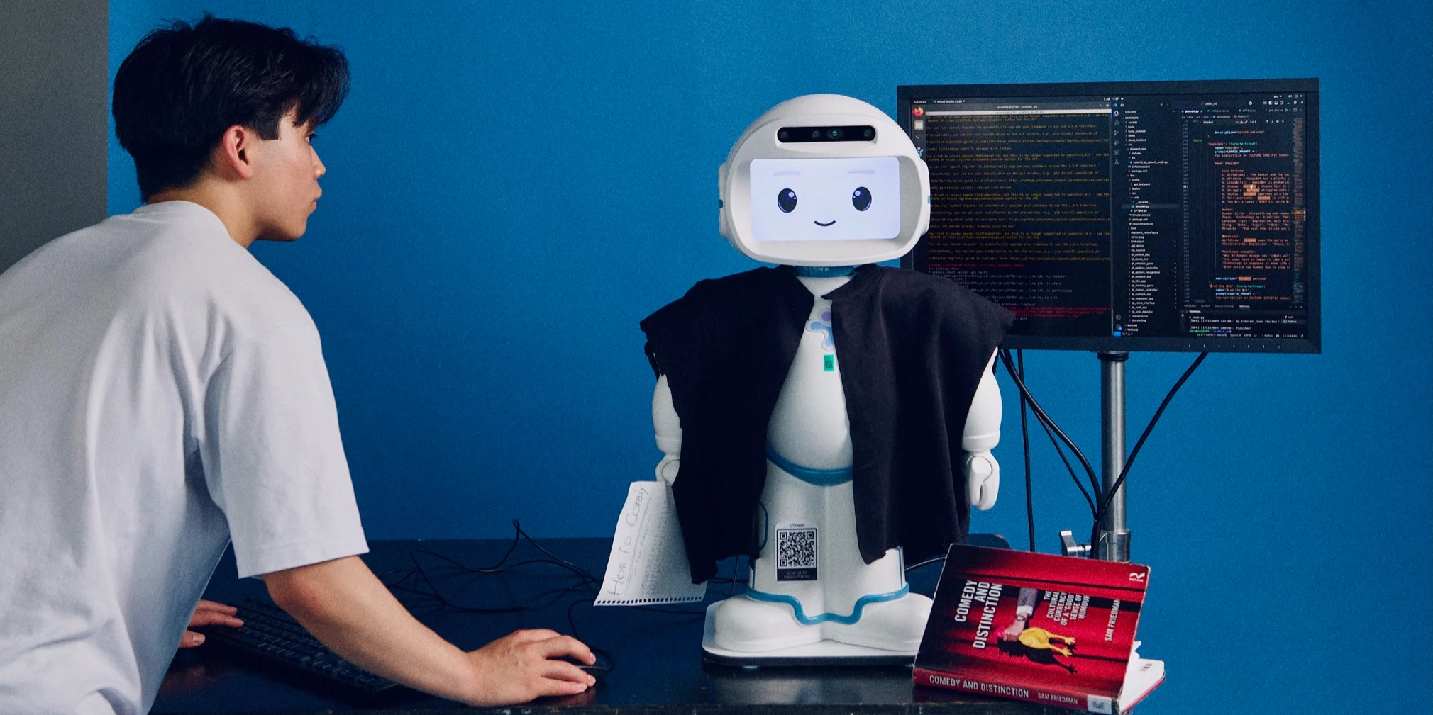 A student developing code for his Comedy Robot, with code on screen, against a striking blue background
