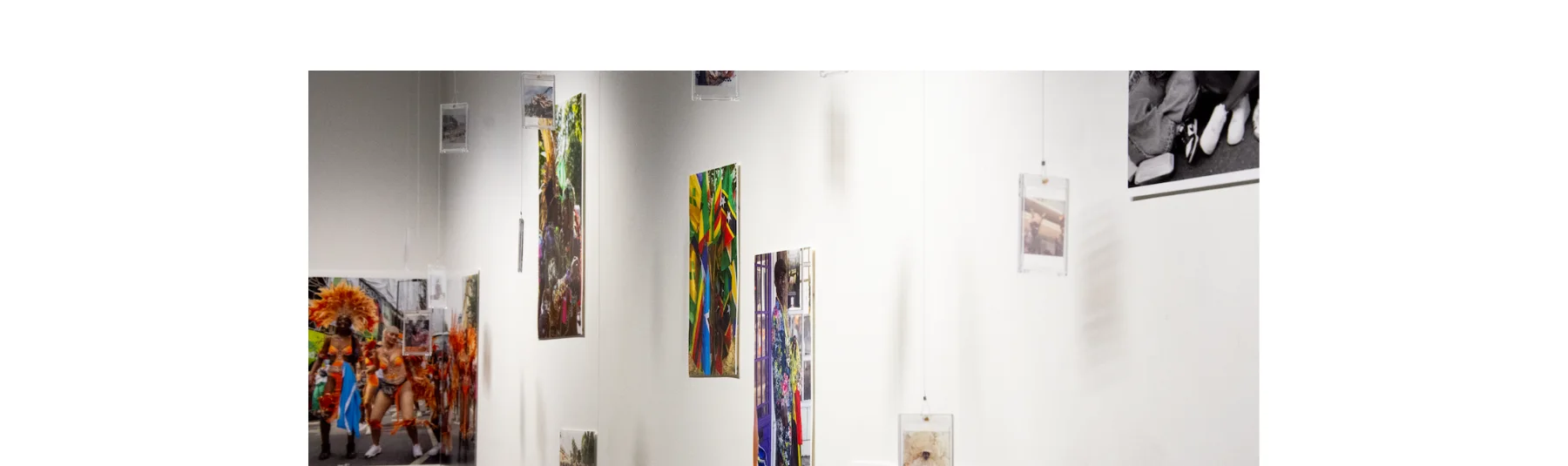 Hanging and pinned up photographic works in different sizes, orientations, colours and formats are on display in an exhibition. Overall they suggest a theme of Carnival.