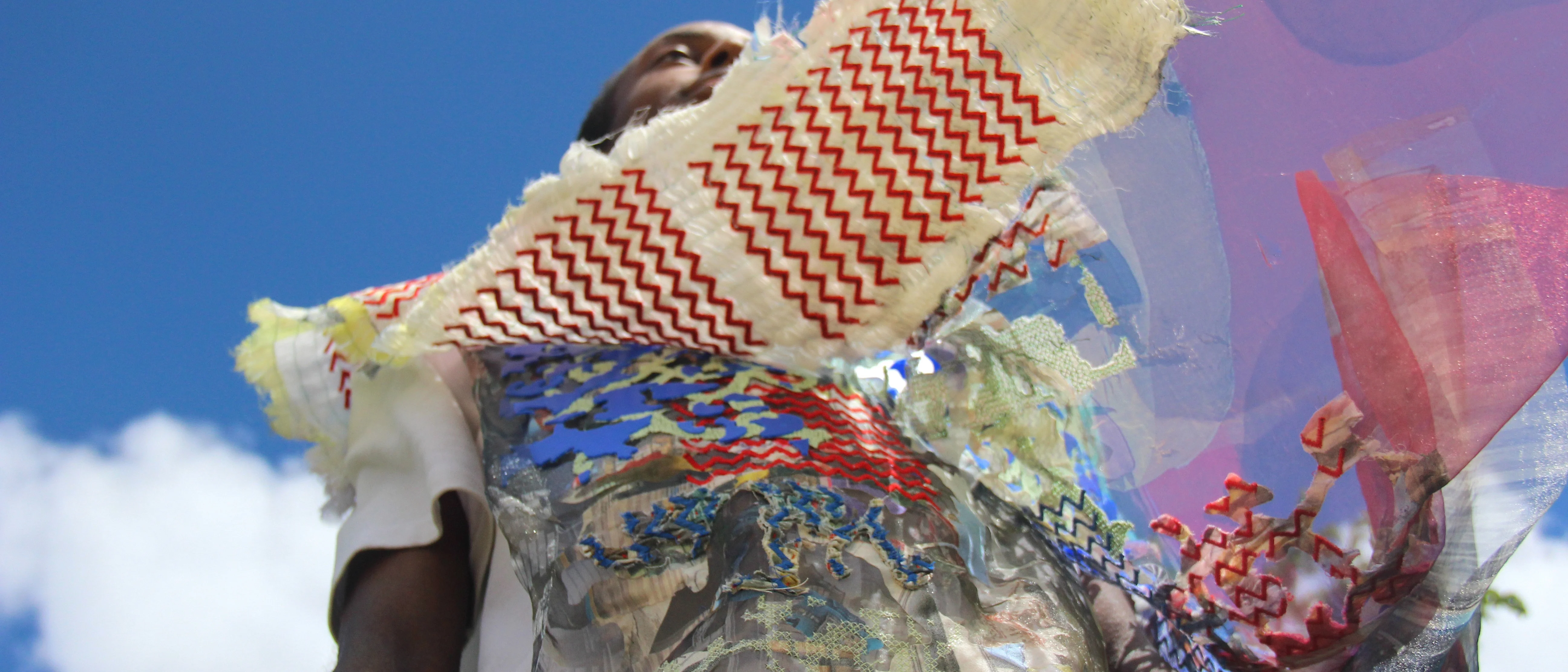 Person wearing a vibrant, abstract outfit with metallic textures and zig-zag patterns, set against a clear blue sky. The mood is bold and artistic.