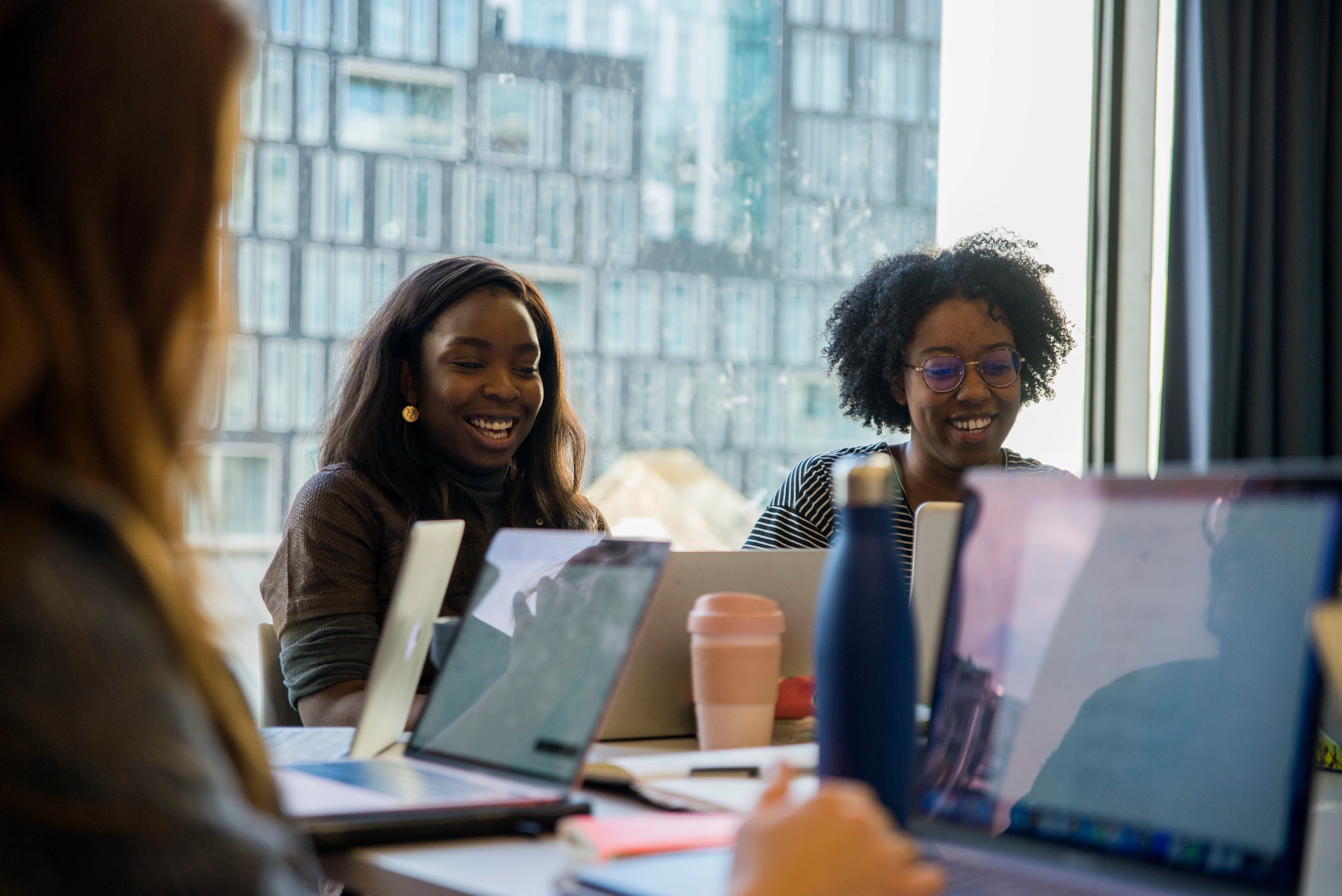 Two young women laughing and looking at their laptops