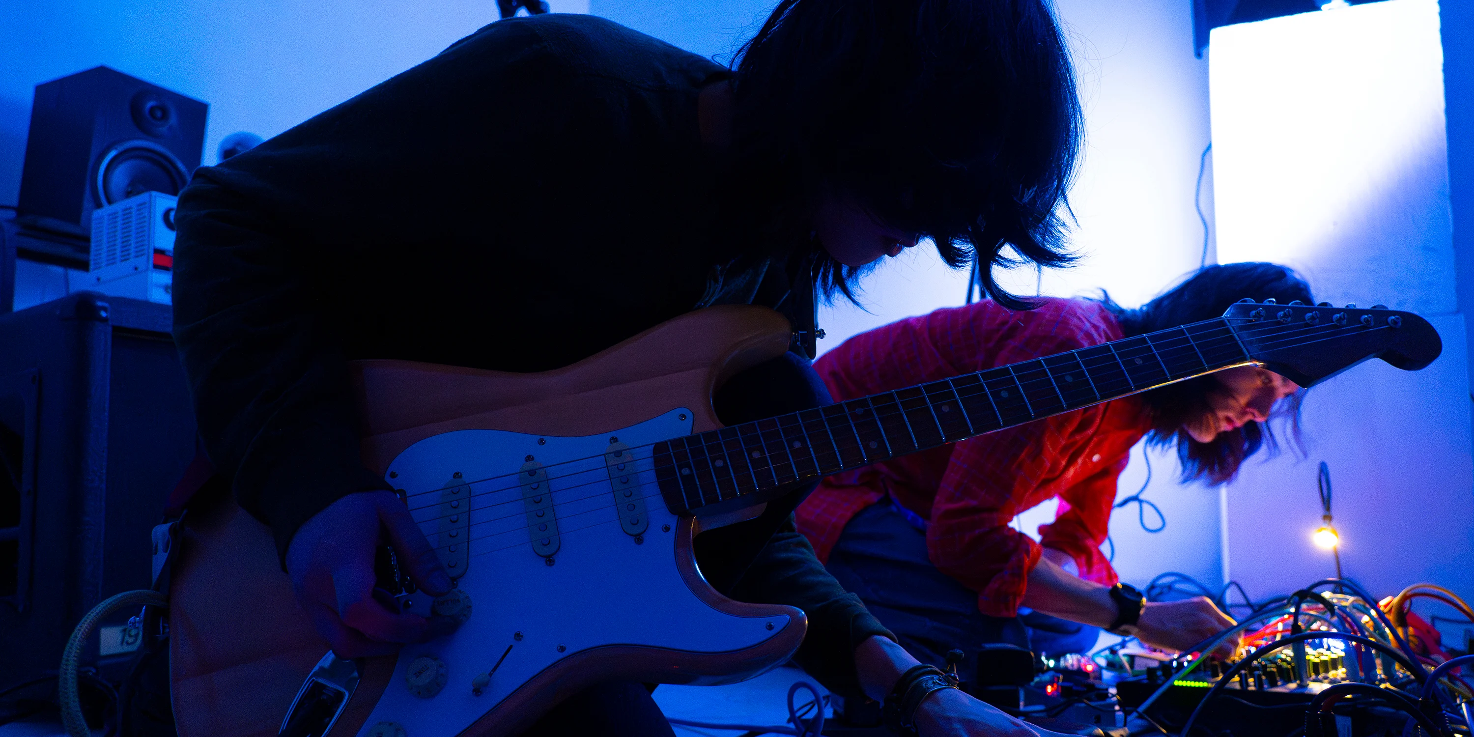Photo of two students playing guitars in a blue dark light.