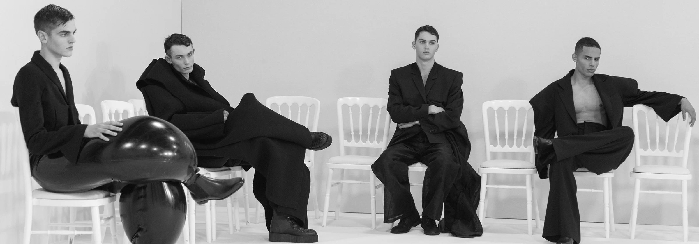 Four male models seated in loose black clothing