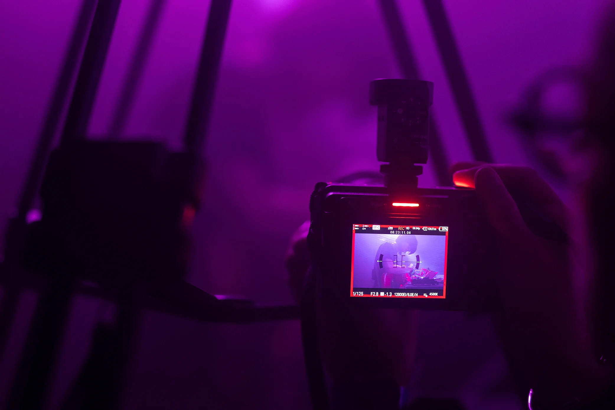 A camera viewfinder shooting a live act on stage, purple stage lighting fills the shot