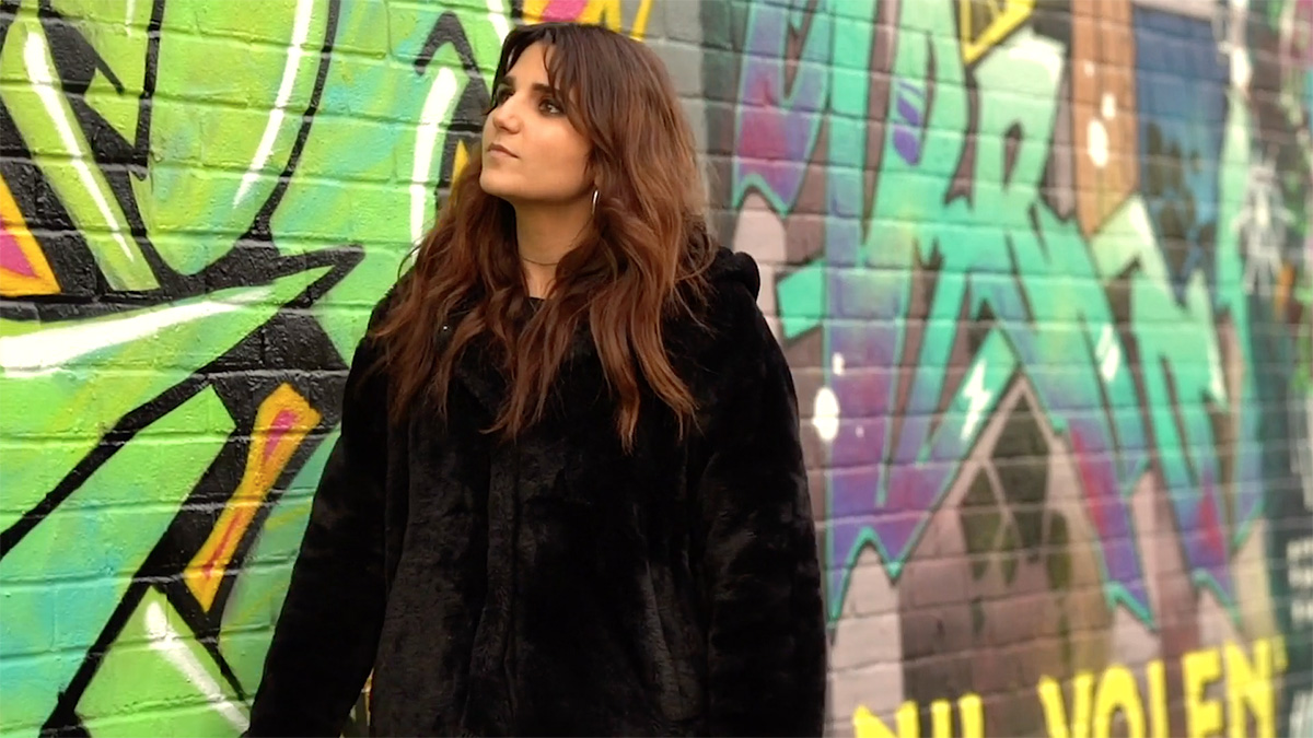 Revital stands in front of a heavily graffiti-ed brick wall.