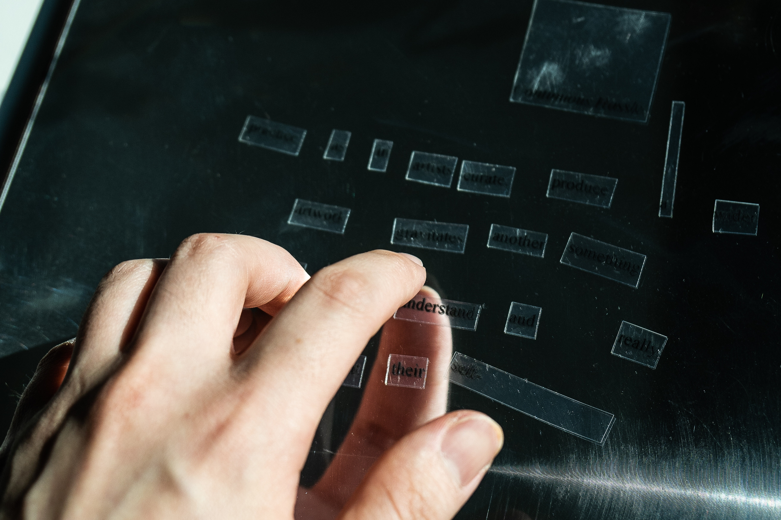 A hand hovering over a mirror with small pieces of plastic with words on them like magnetic poetry