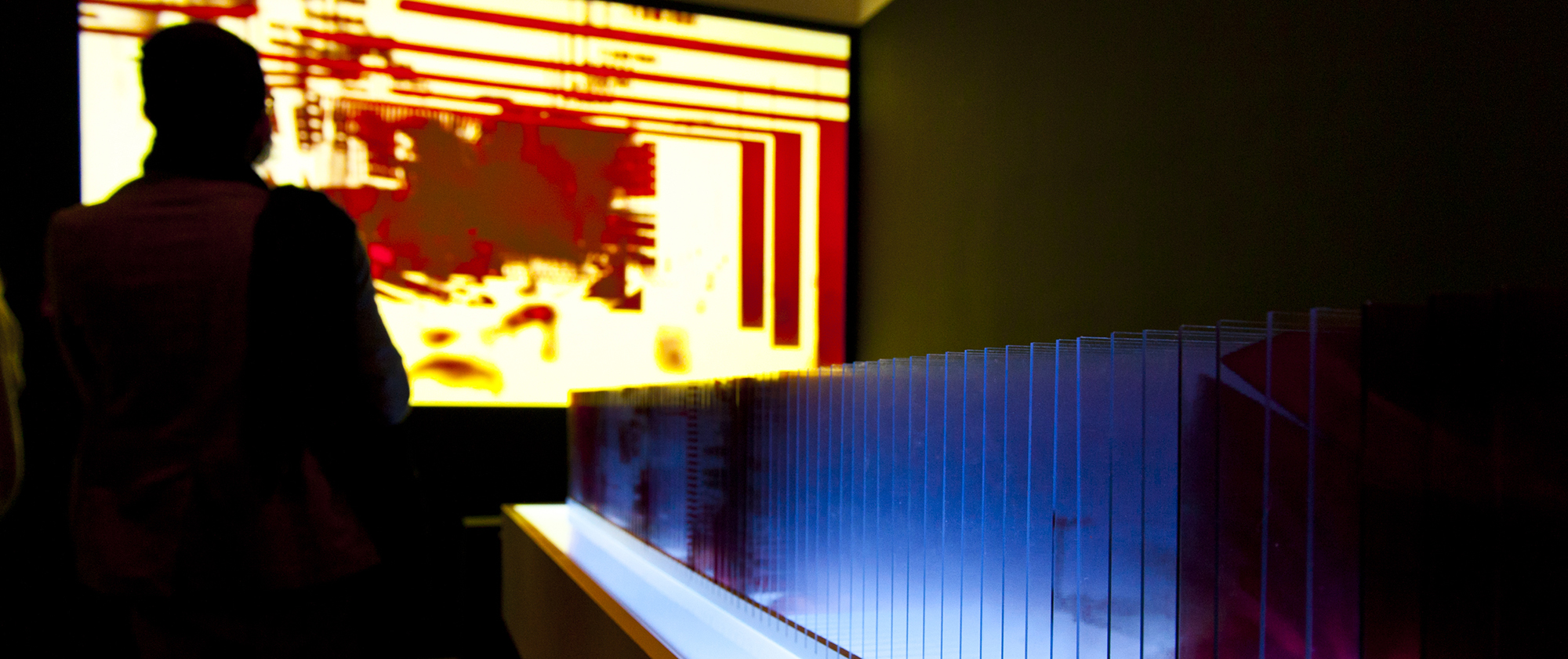 A silhouetted figure stands in front of a red and yellow screen.