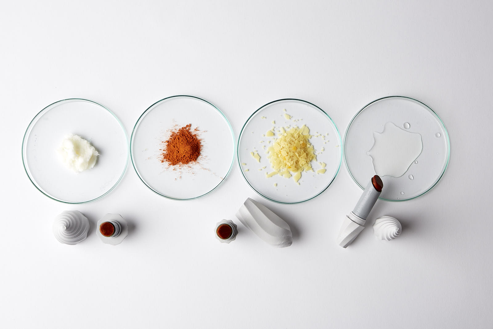 Petri dishes holding coloured powders with lipstick tubes beside
