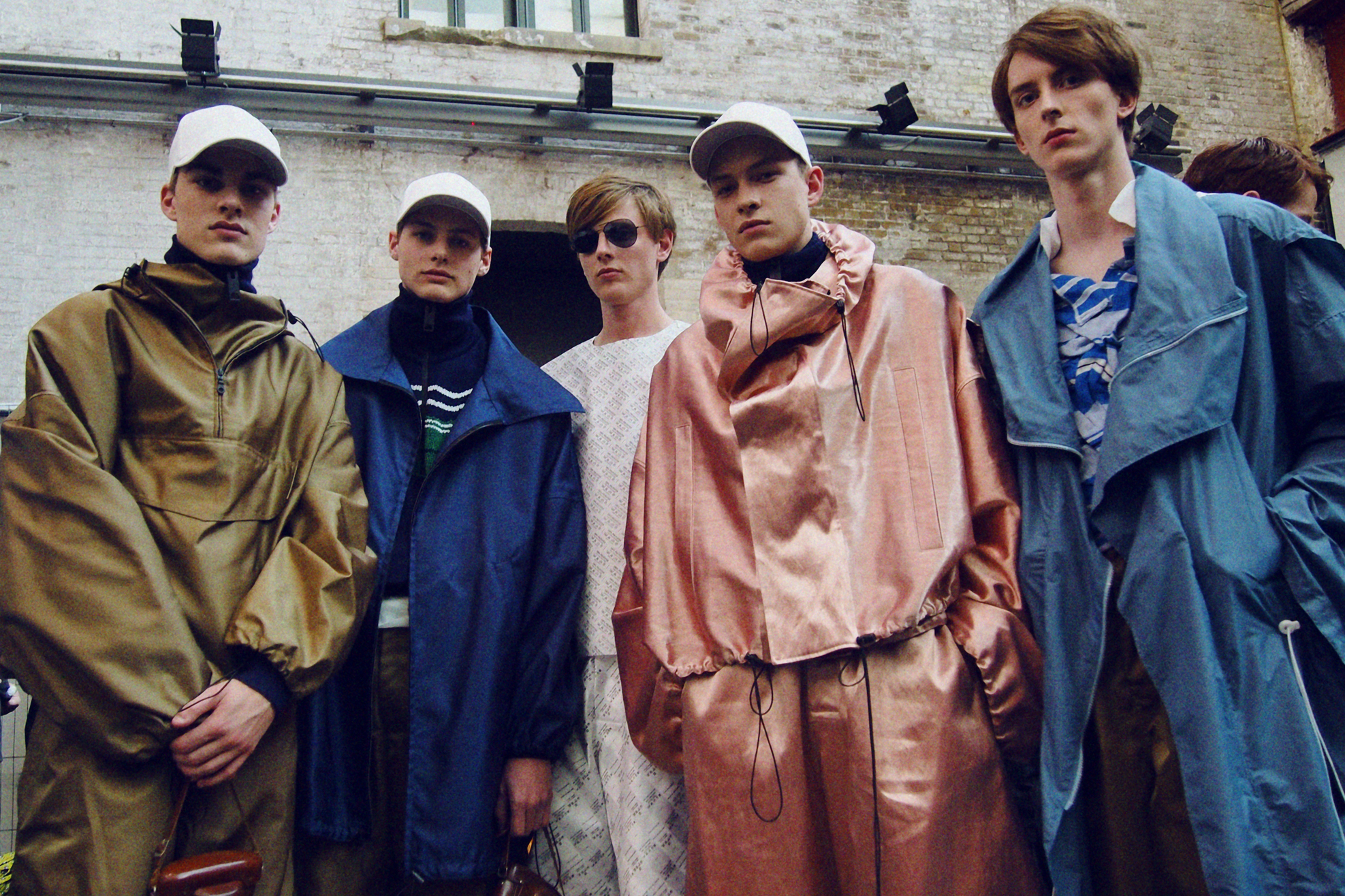 Five male models, some wearing baseball caps and some wearing sunglasses 
