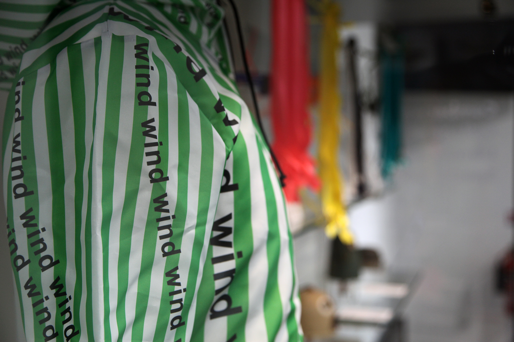 Exhibition display cabinet with a detail of a special green and white striped suit featuring text which reads 'wind' repeatedly.