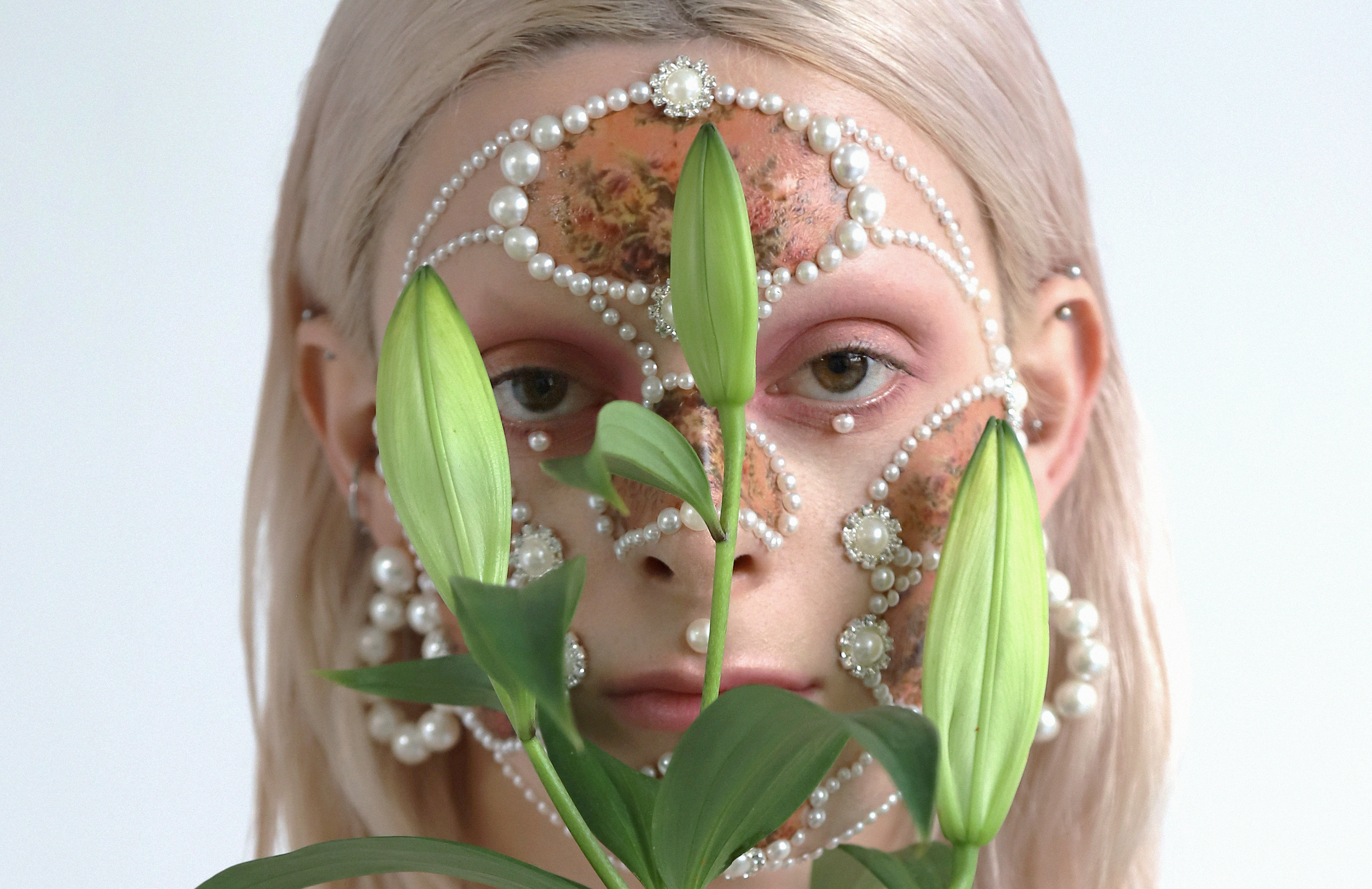 Female model with pearl facial jewellery, makeup and lilies.