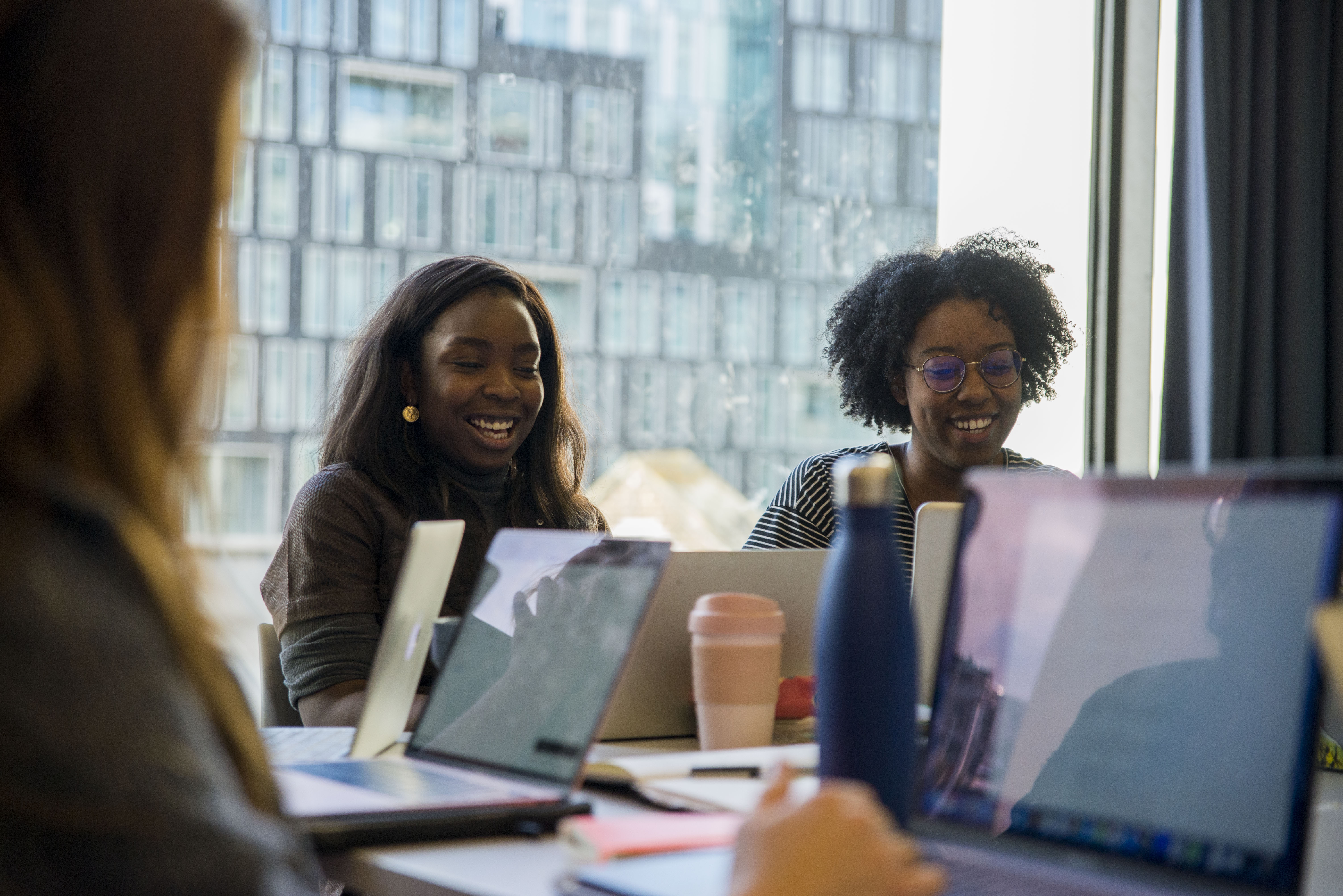 Two young women laughing and looking at their laptops