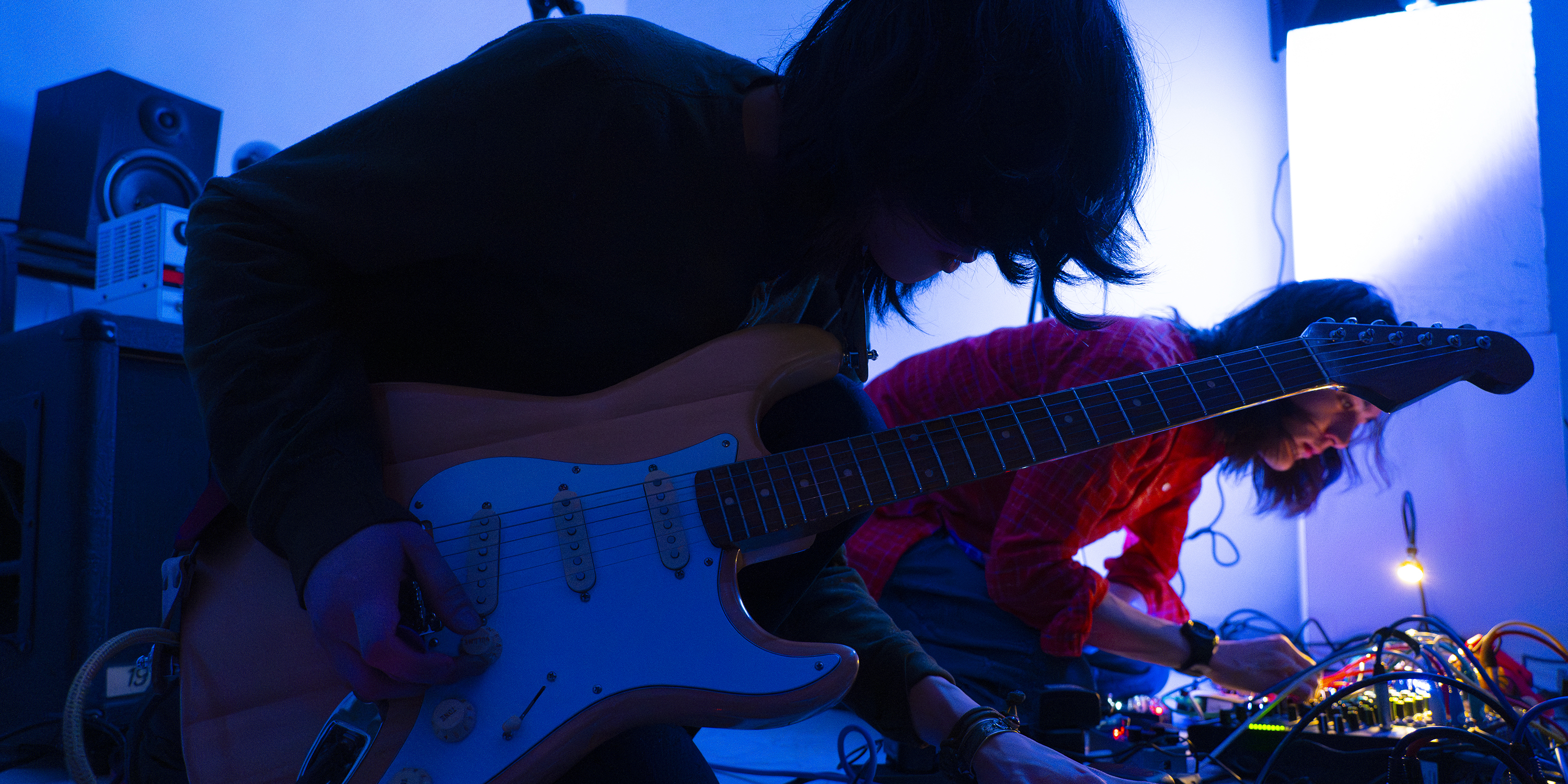 Photo of two students playing guitars in a blue dark light.