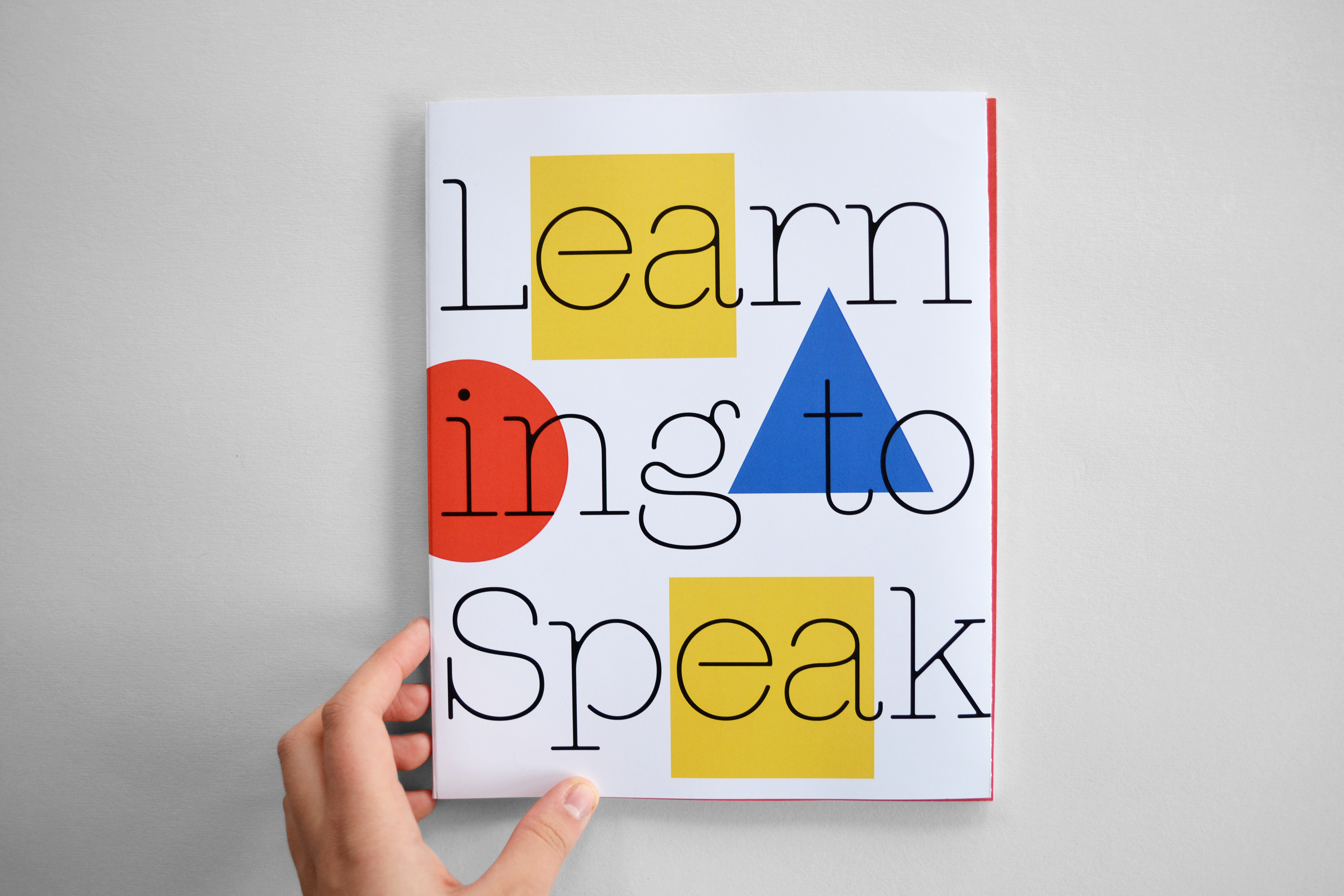 A hand holds small book with colourful shapes. Text reads 'learning to speak' 