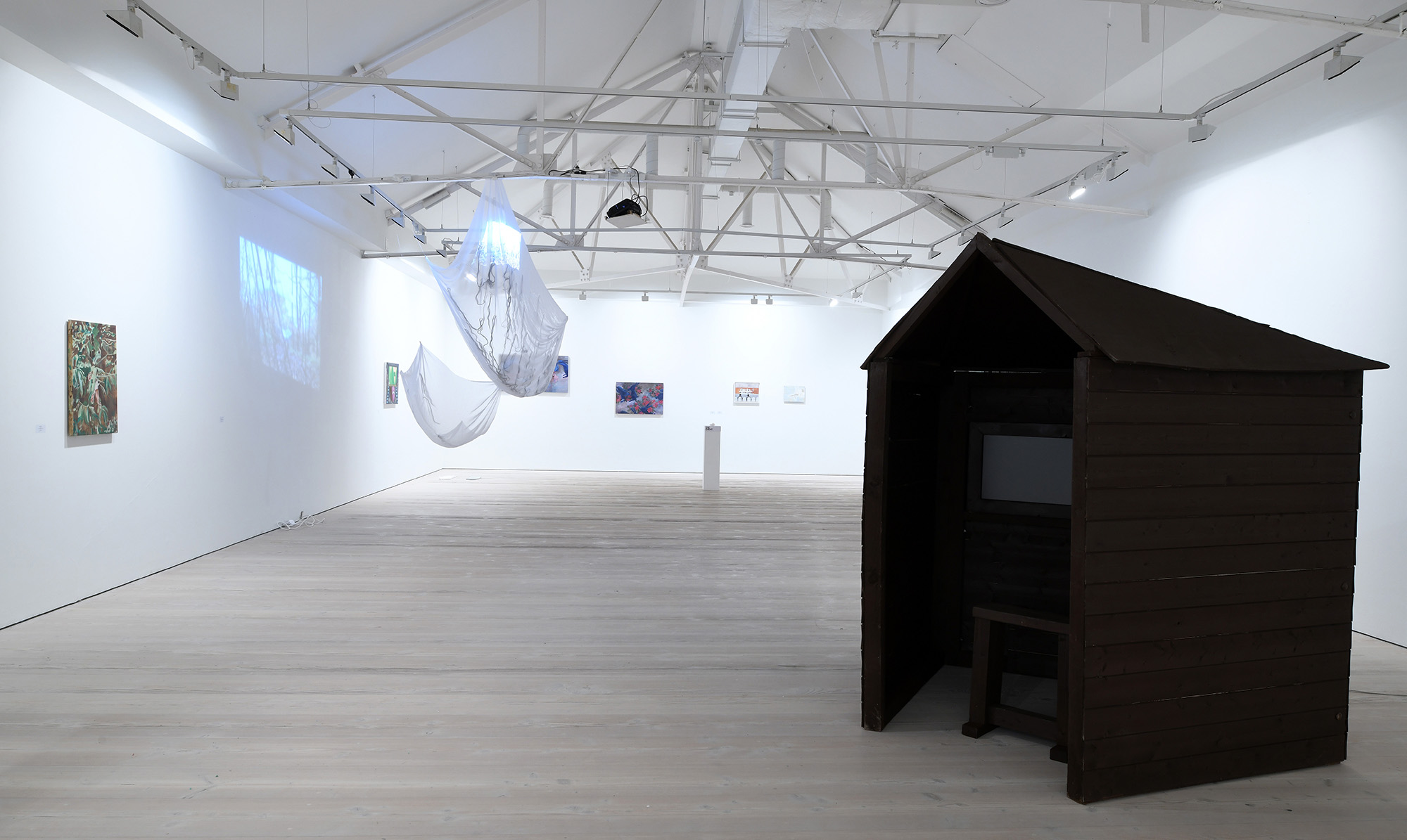 Gallery space with large black shed and paintings on wall