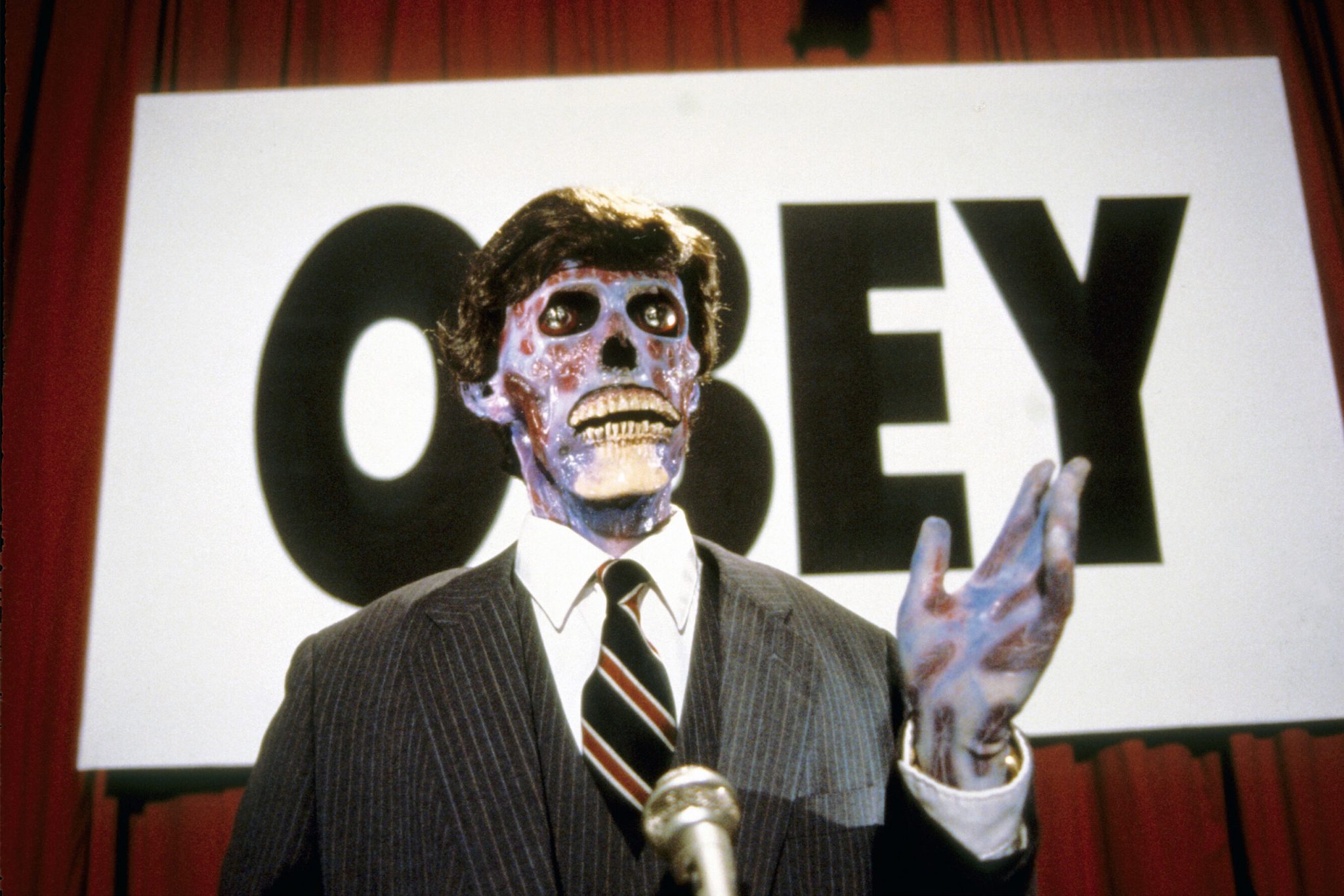Skeleton in a suit next to sign that reads 'OBEY' 