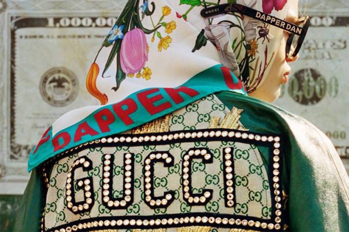 Female model wearing Dapper Dan sunglasses and scarf with paper bill in the background. 