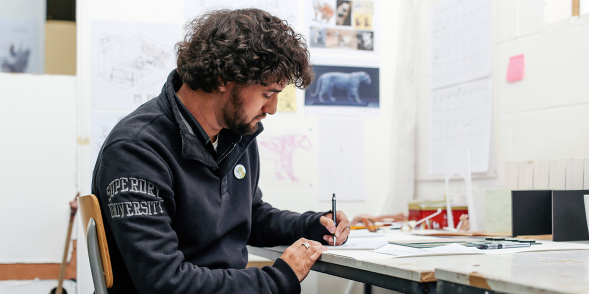 Student sitting at work bench and sketching in studio.