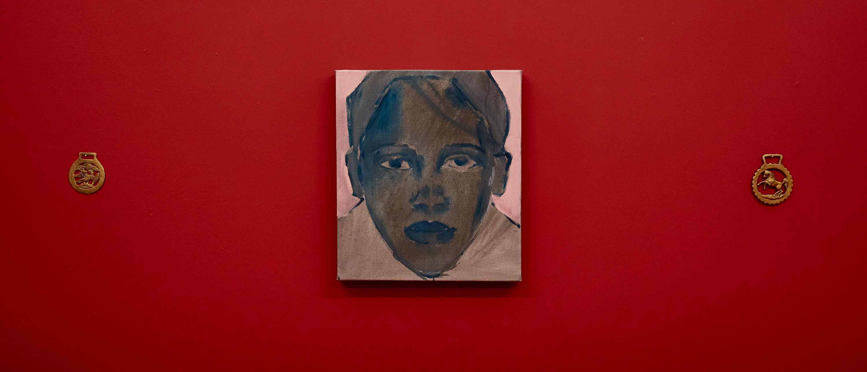 Installation with painted red background with painting of a portrait in the centre with brass objects hung either side. Work by Stevie Ray Latham - MA Fine Art: Painting, Camberwell College of Arts.