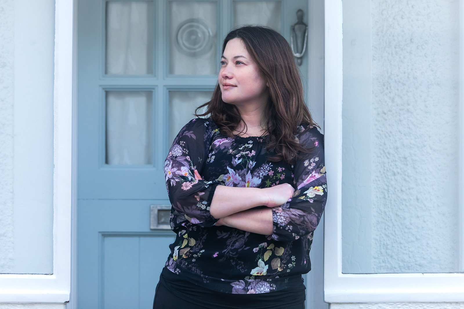 A woman stands in front of a door and looks away from the camera.