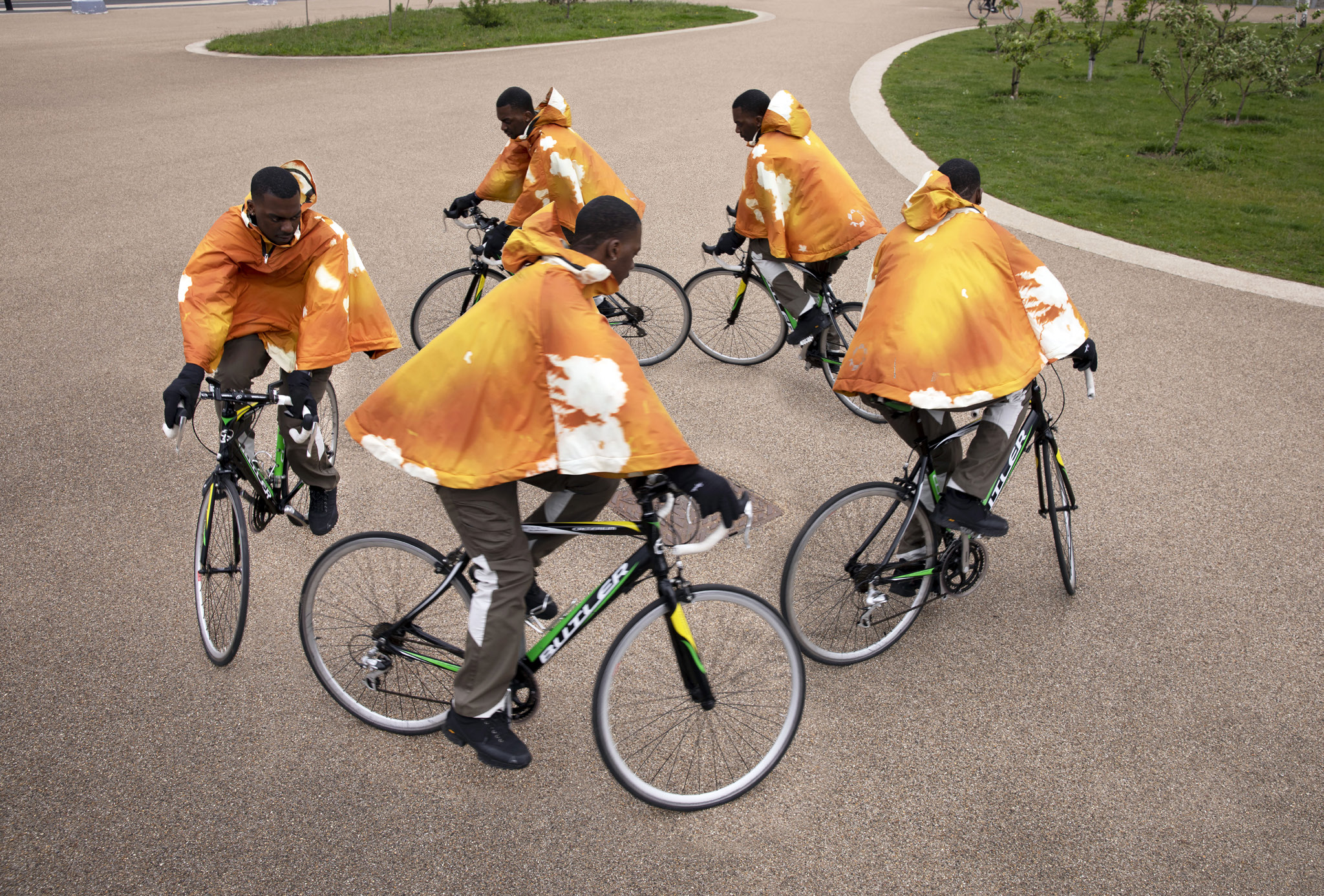 Five black male cyclists wearing orange hoodies.