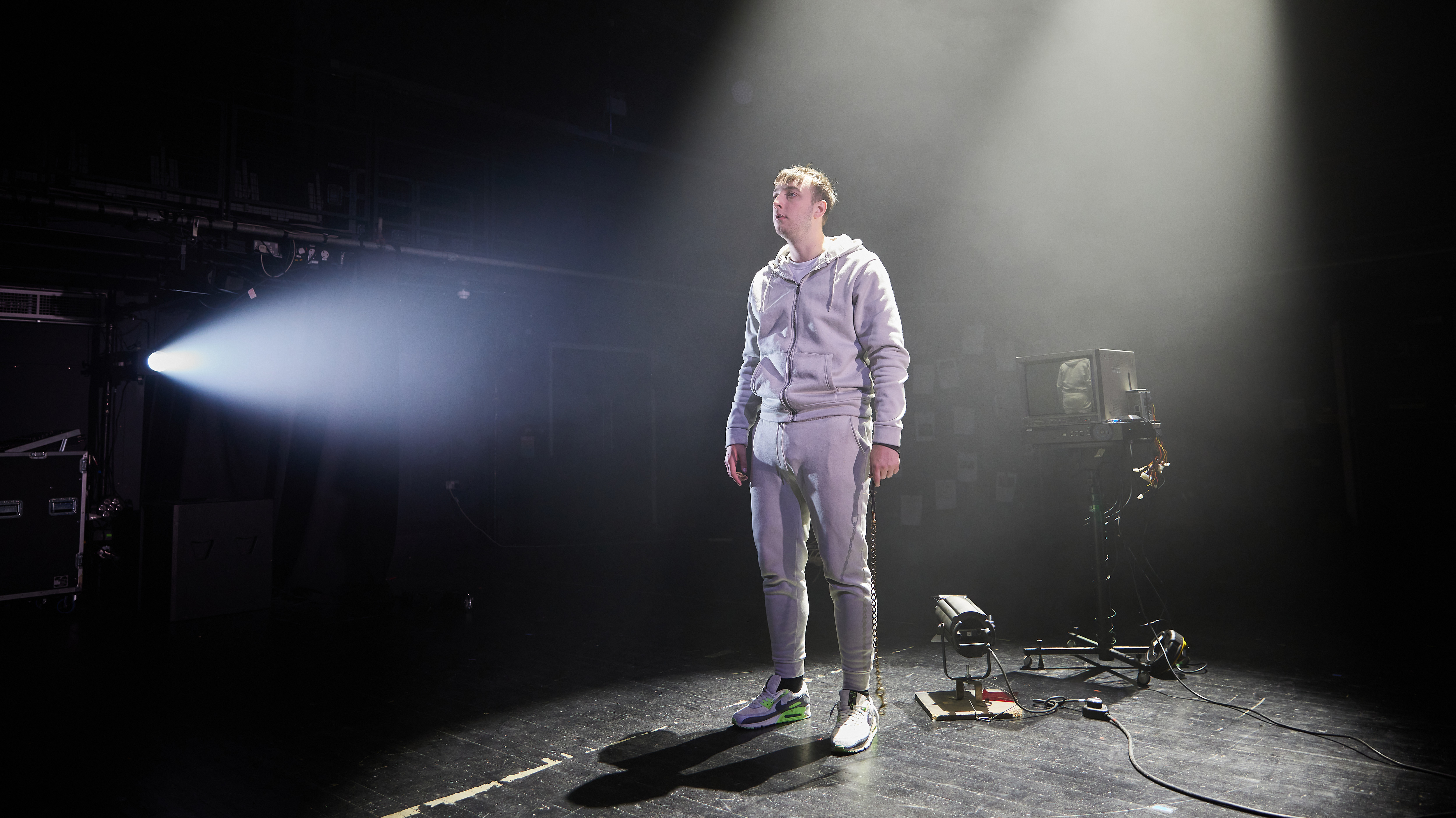 Boy wearing a grey tracksuit and Nike Air Max trainers standing in front of a television monitor.