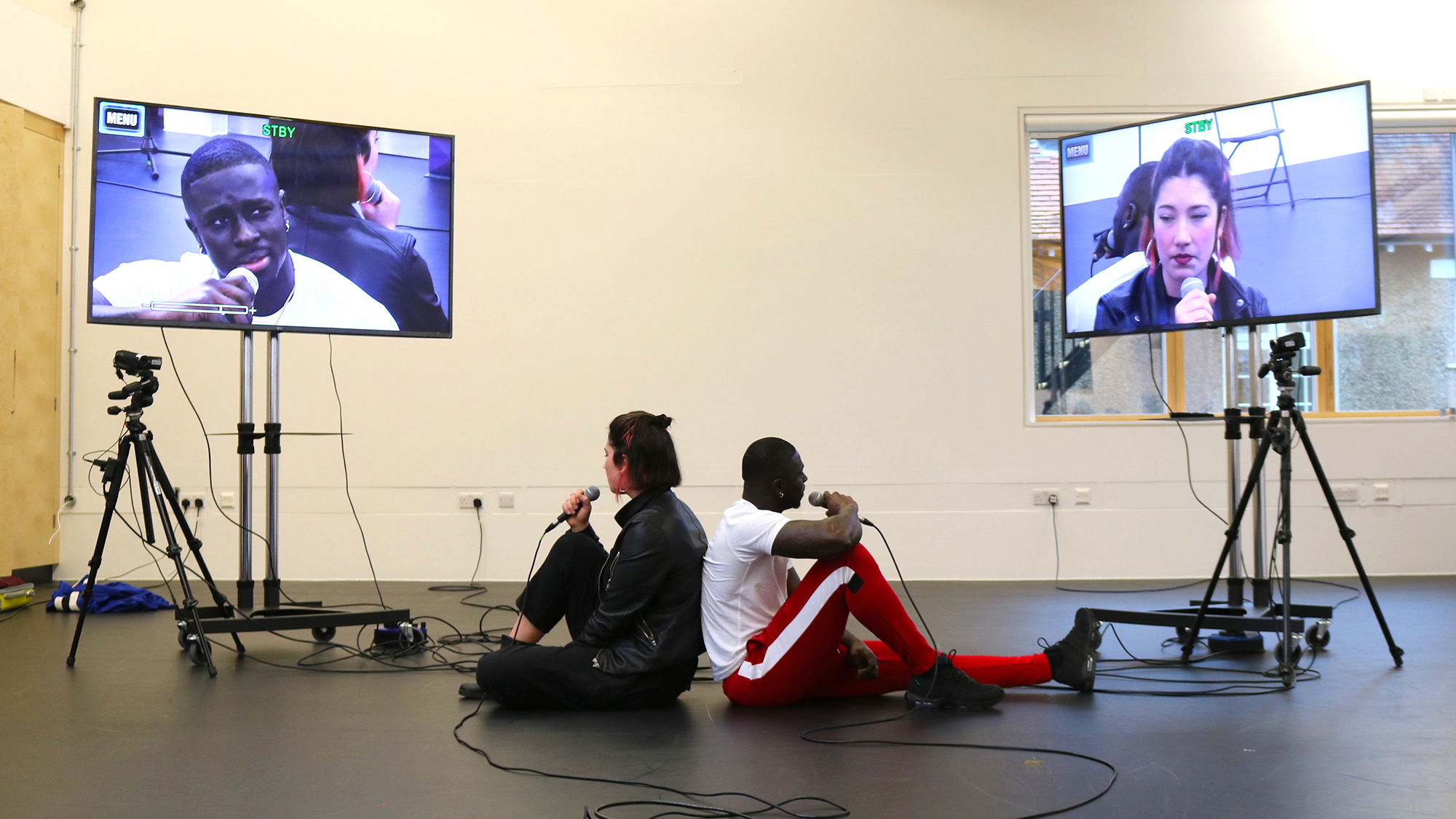 BA Contemporary Theatre and Performance students performing with microphones and 2 large screen televisions in the acting lab session.