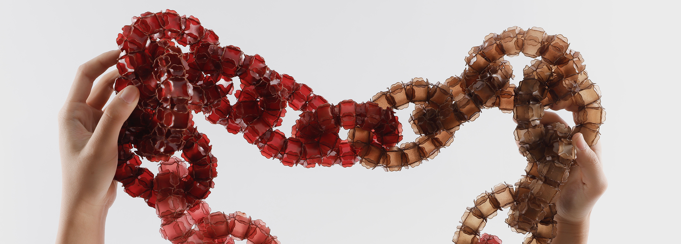 Two hands holding up a red-coloured interlinked piece of jewellery.