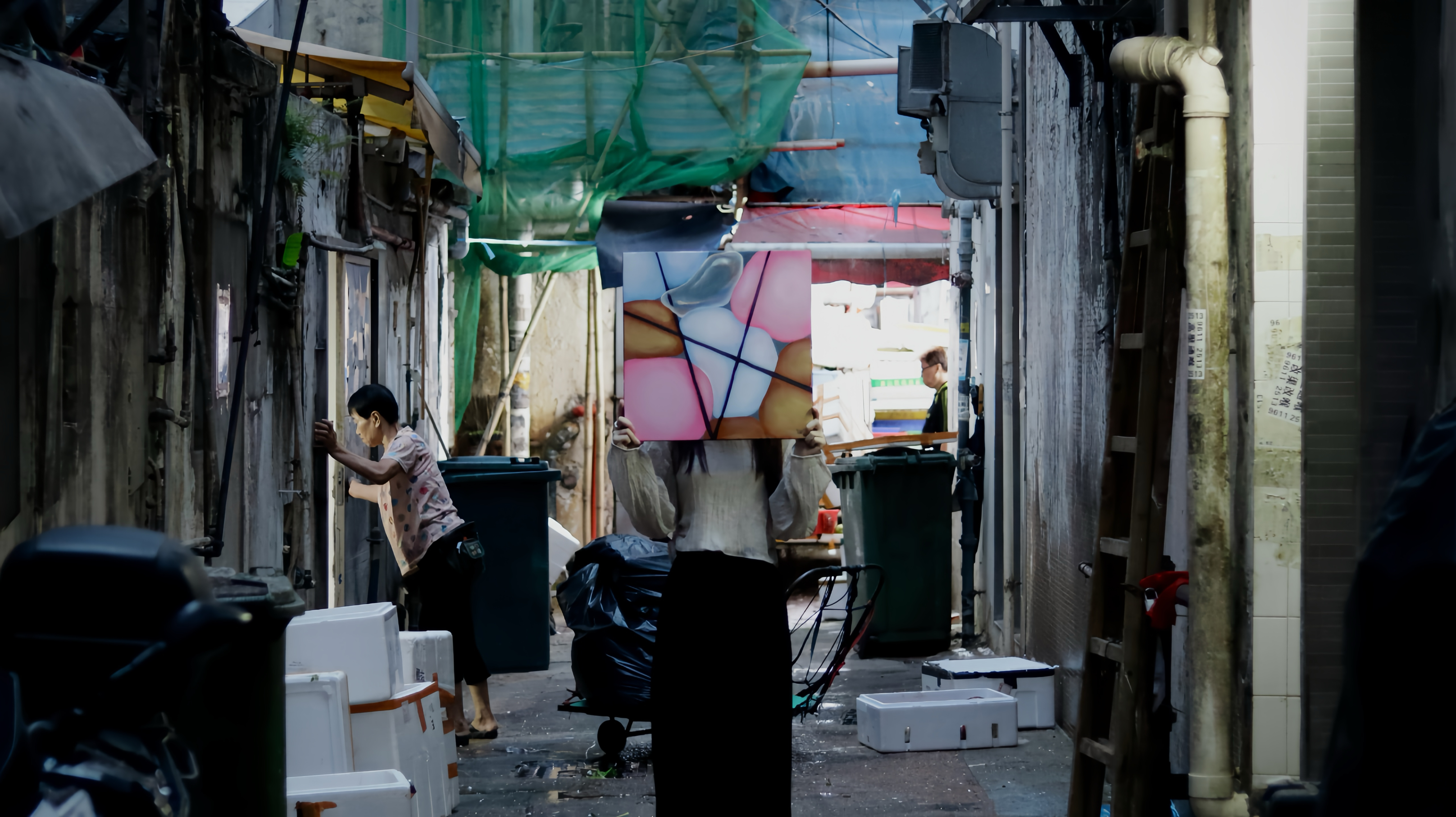A photo pf a person holding up an artwork in front of their face against the backdrop of an outdoor market