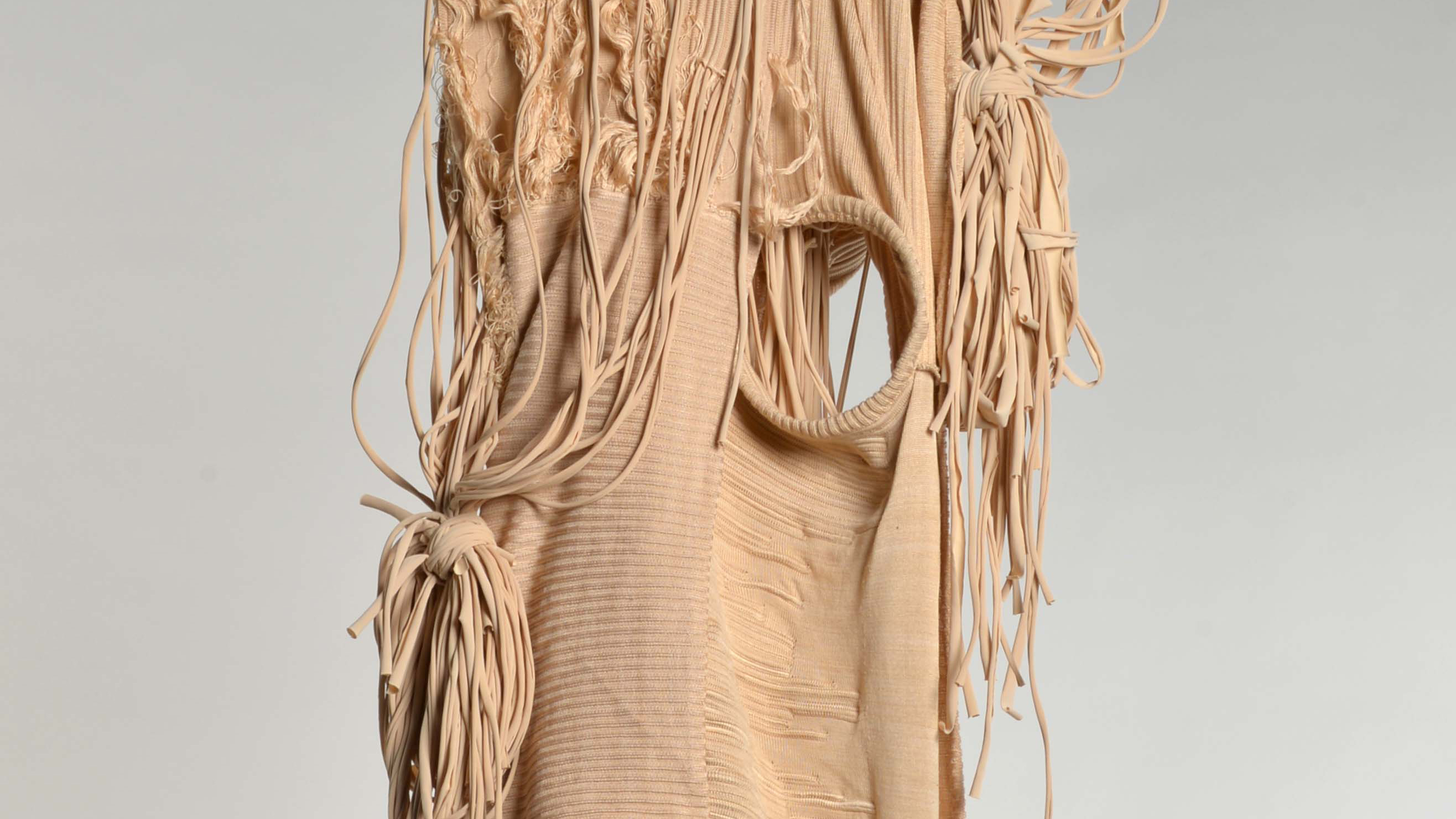 Contemporary hanging textile sculpture in a muted warm earthy colour consisting of a central panel with knotted fabric strands. By Mila Harris-Mussi.