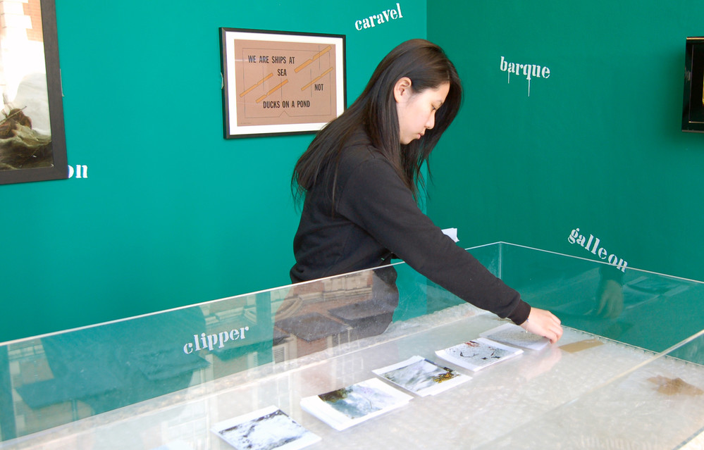 An Asian student setting up materials in an exhibition display against a forest green wall